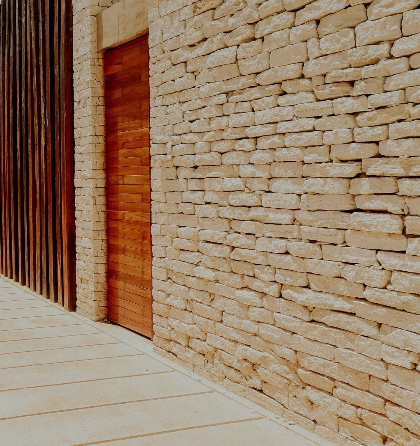 Stacked natural stone beside warm timber slats and a wood door in raking light
